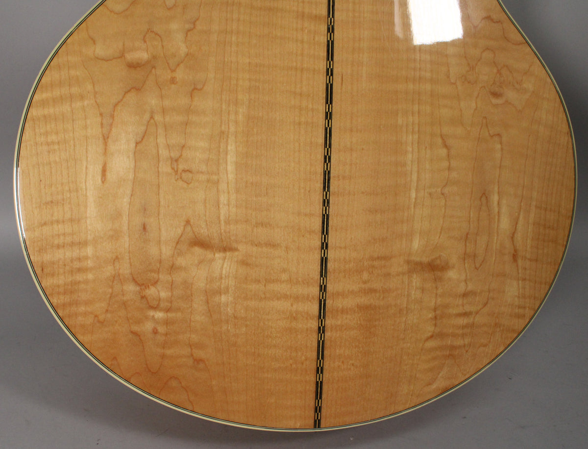 The back of the natural finish acoustic guitar, showing the light wood grain with a dark center strip and light binding around the edge.