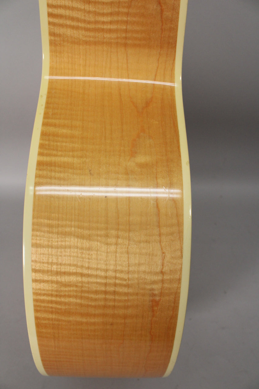 Close-up of the guitar's light-colored, highly figured maple side, showing a few small dings along the cream binding.