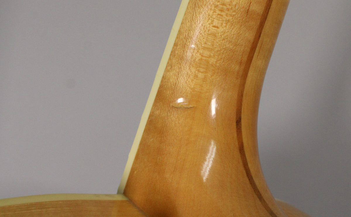 Close-up of the guitar's natural finish neck heel, showing a small ding on the upper curve and light wood grain.