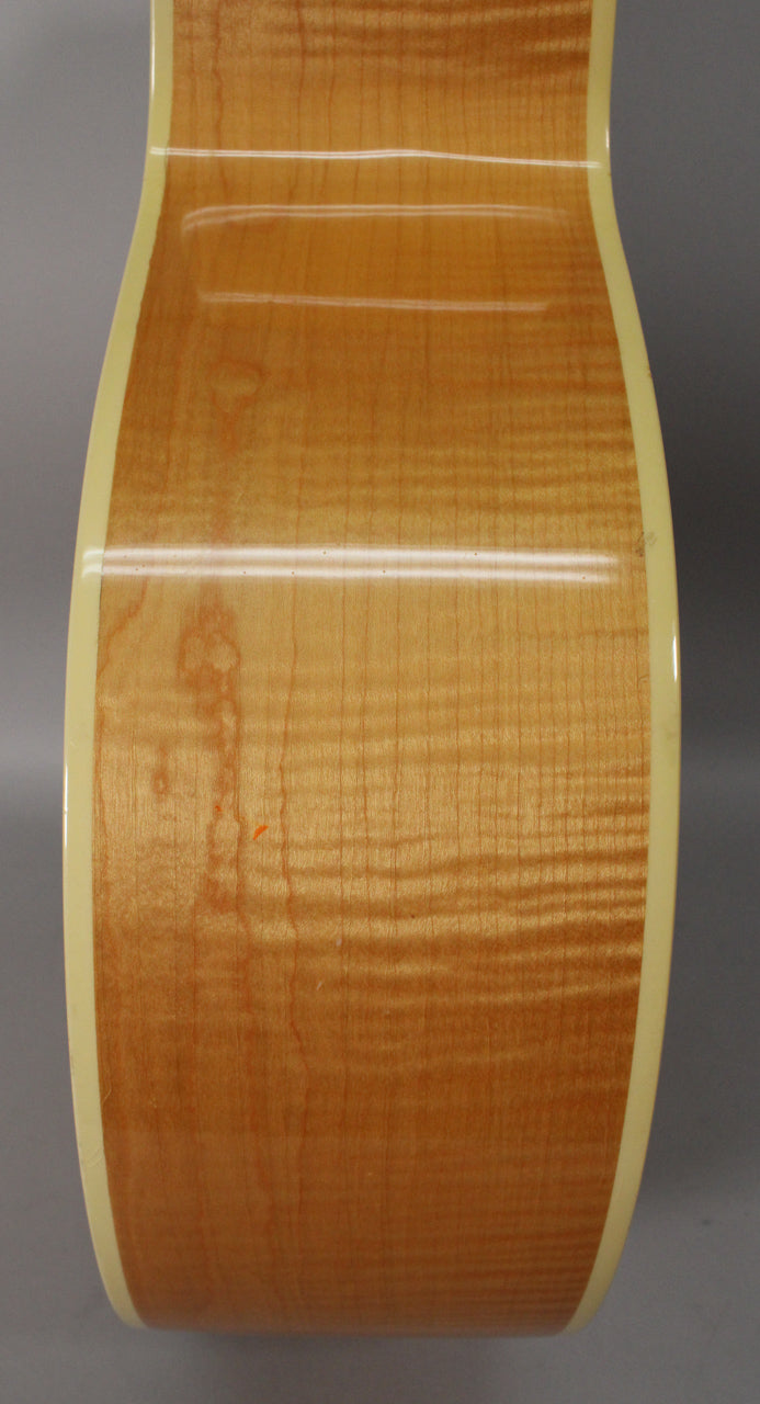 The guitar's light brown, flame maple side with cream binding shows some finish wear and a small orange mark near the waist.