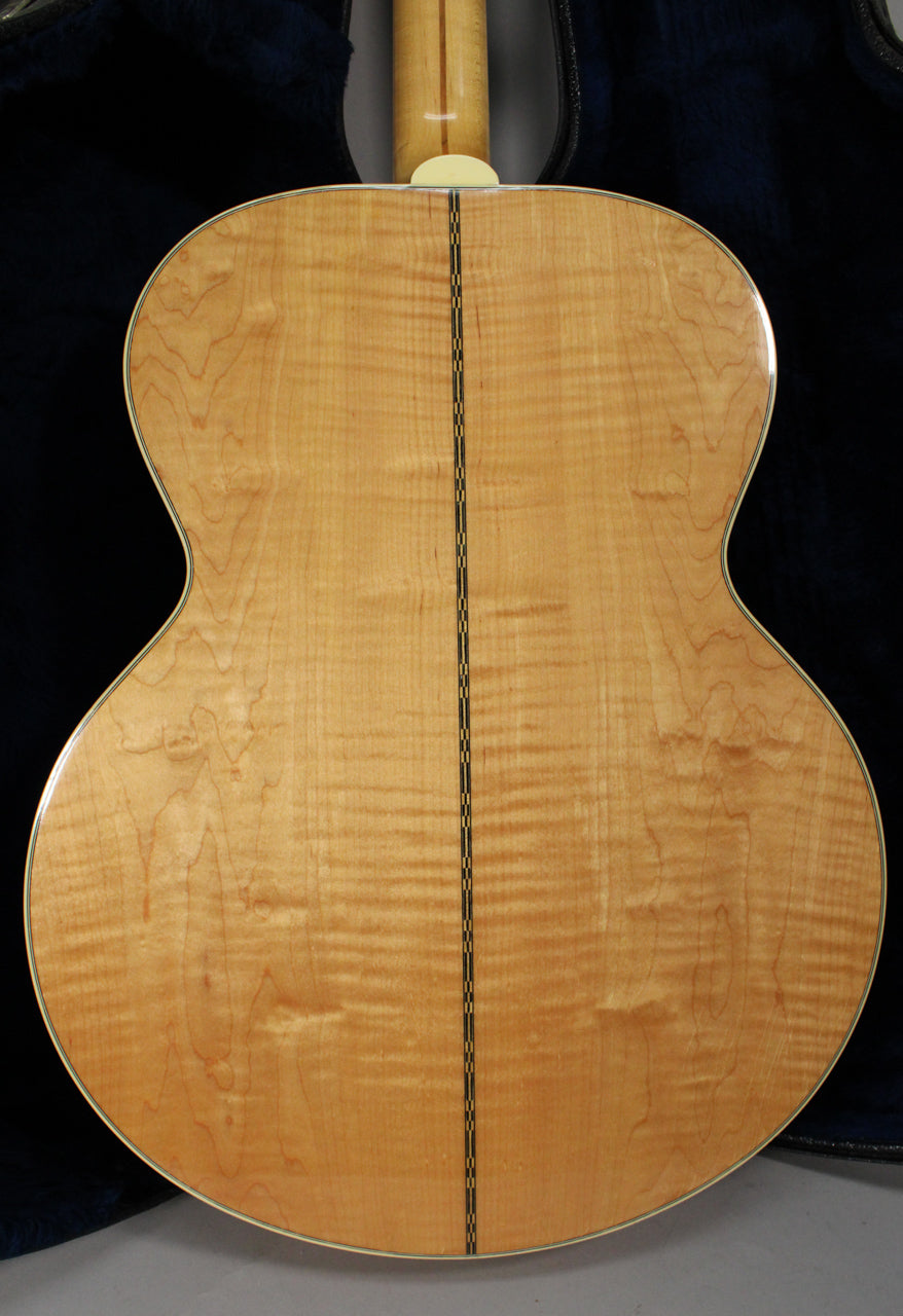 The back of the natural finish acoustic guitar shows a flamed maple grain, a checkered center strip, and a cream heel cap.