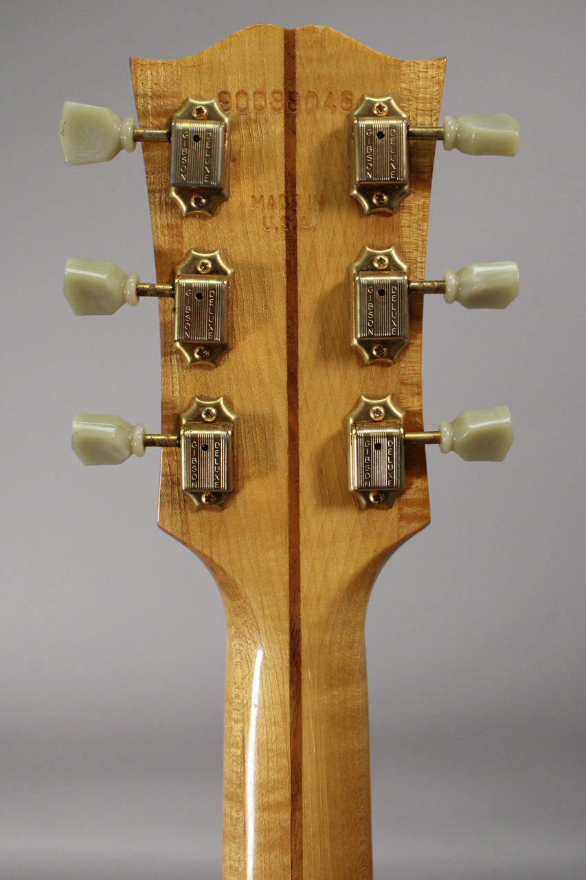 The back of the headstock and upper neck, showing six gold tuners with cream buttons, a serial number, and a dark wood stripe.