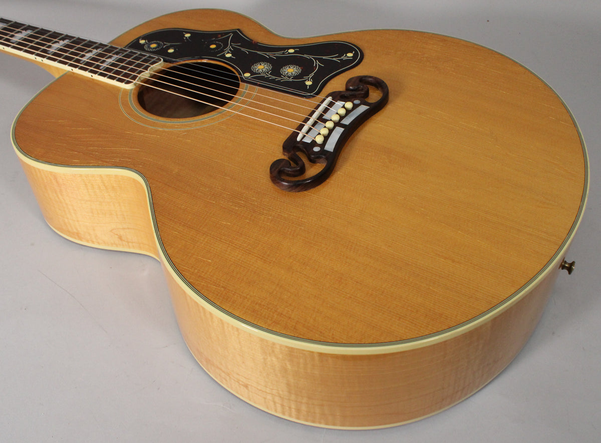 The natural finish acoustic guitar is angled from the upper left, showing the body, pickguard, and ornate bridge.