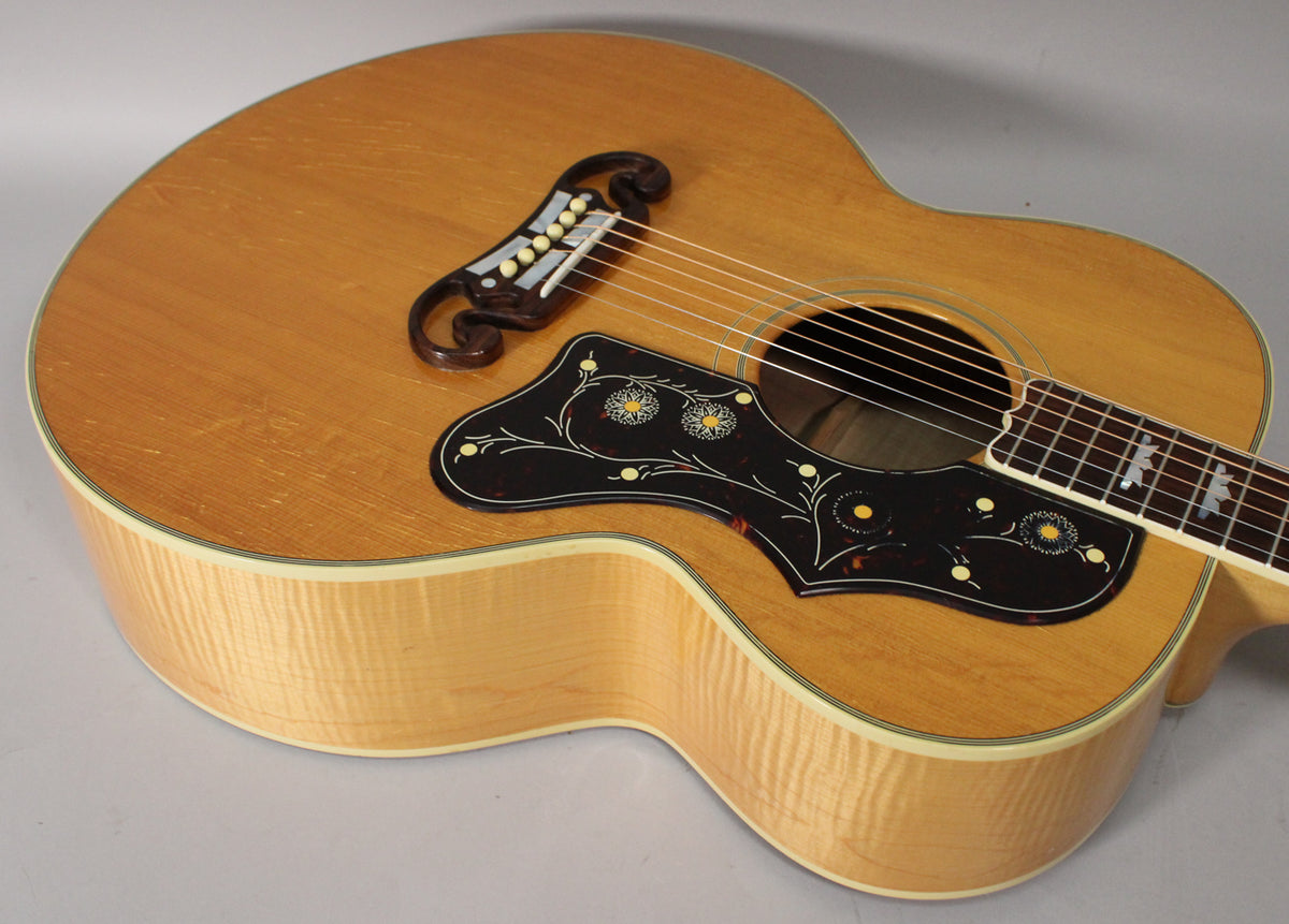Overhead view of a natural finish acoustic guitar, showing the body, ornate pickguard, and bridge with some light wear.