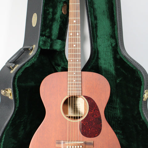 Full-front view of a matte reddish-brown acoustic guitar with a dark tortoiseshell pickguard, standing in an open, dark green plush-lined case.