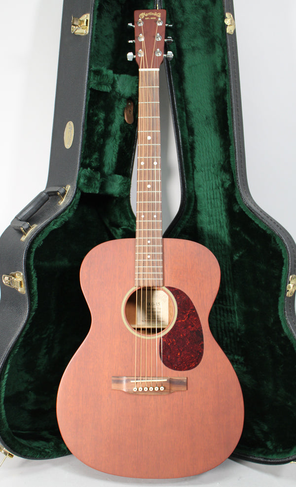 Full-front view of a matte reddish-brown acoustic guitar with a dark tortoiseshell pickguard, standing in an open, dark green plush-lined case.