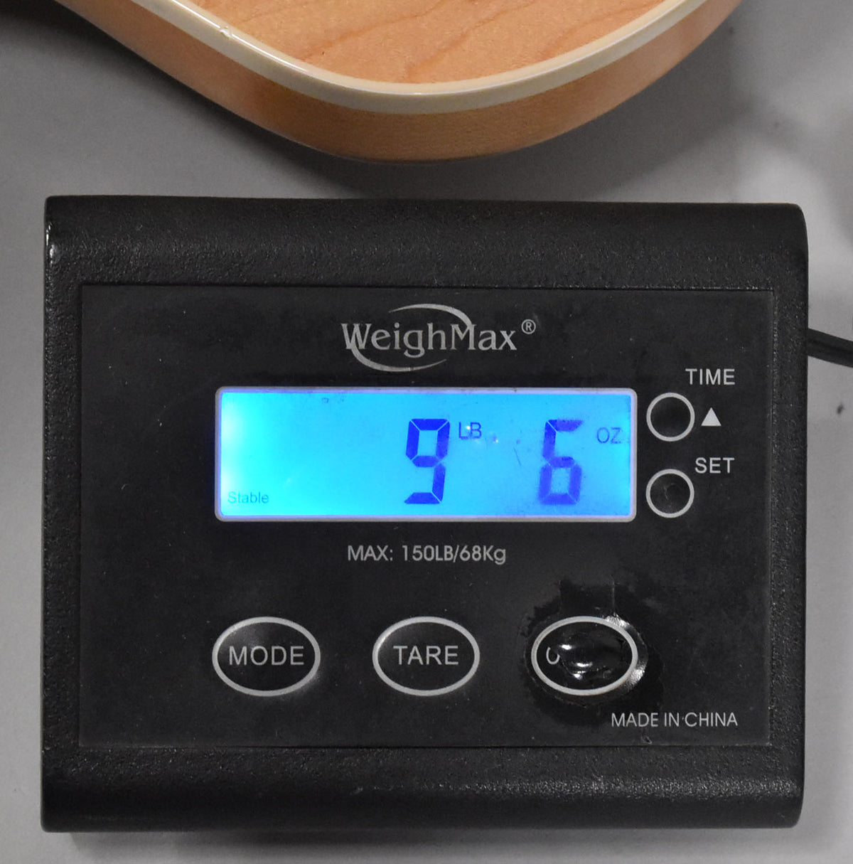 The bass's lower bout, in natural wood with cream binding, rests on a black digital scale displaying "9 LB 6 OZ".