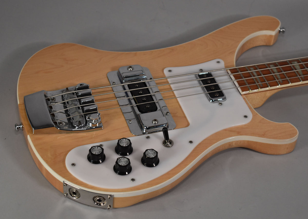 The natural finish bass body, with white binding and pickguard, is angled to show the chrome bridge, pickups, and four black control knobs.