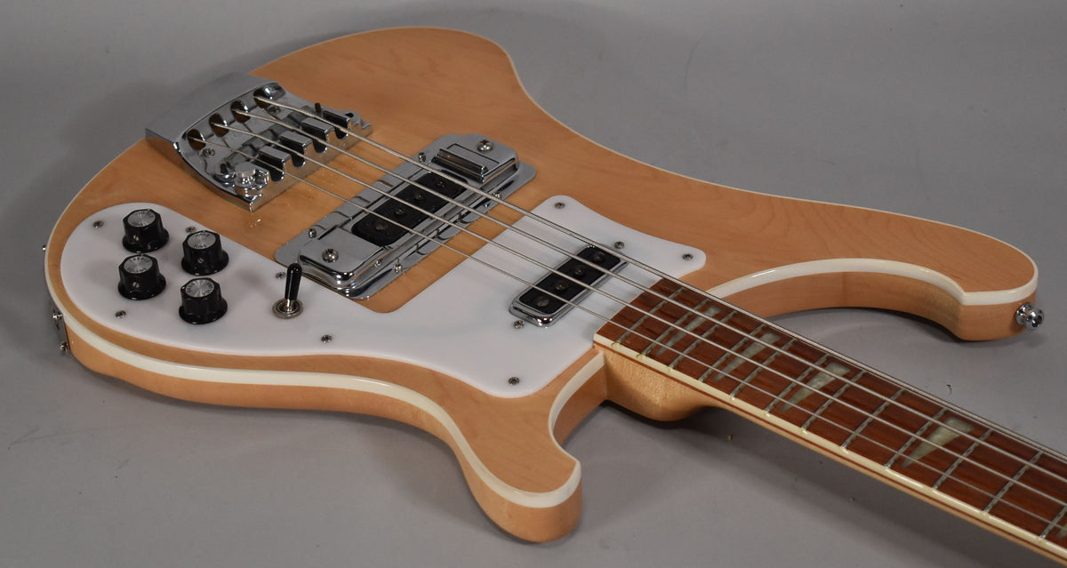 The natural maple bass body, with white binding and pickguard, is angled to show the chrome bridge, pickups, and control knobs.