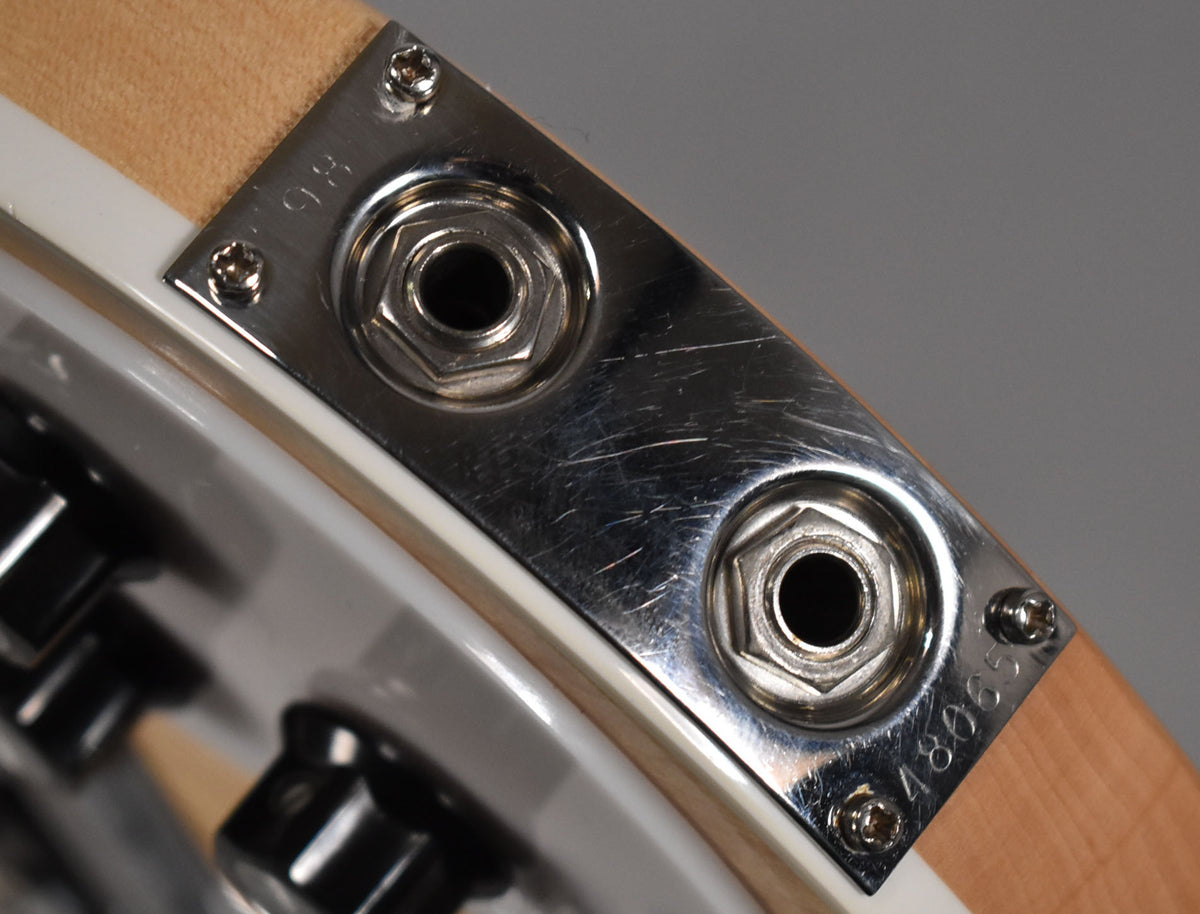Close-up of the chrome output jack plate, showing two jacks and many surface scratches, mounted on the bass's maple body.