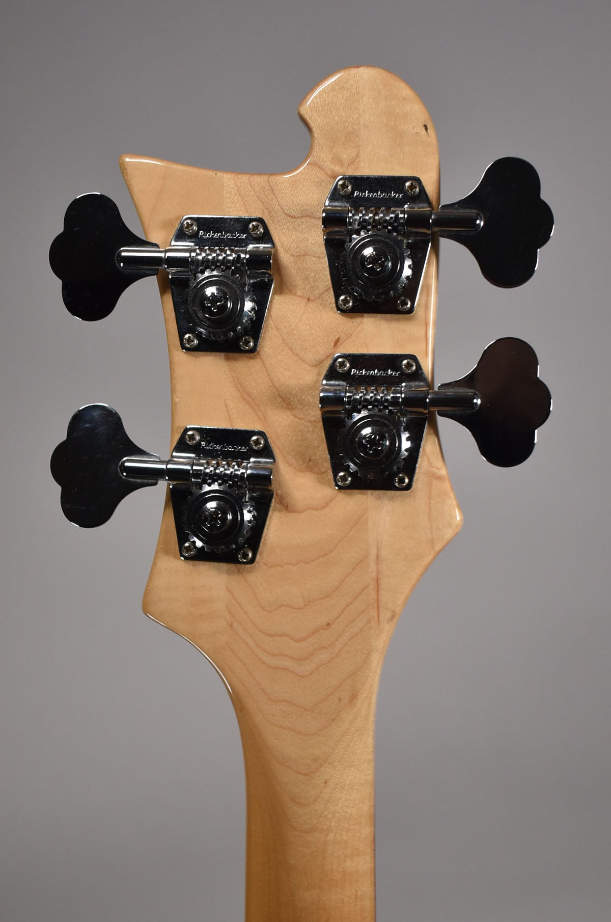 The bass's natural maple headstock and neck are shown from behind, with four chrome clover-leaf tuners.