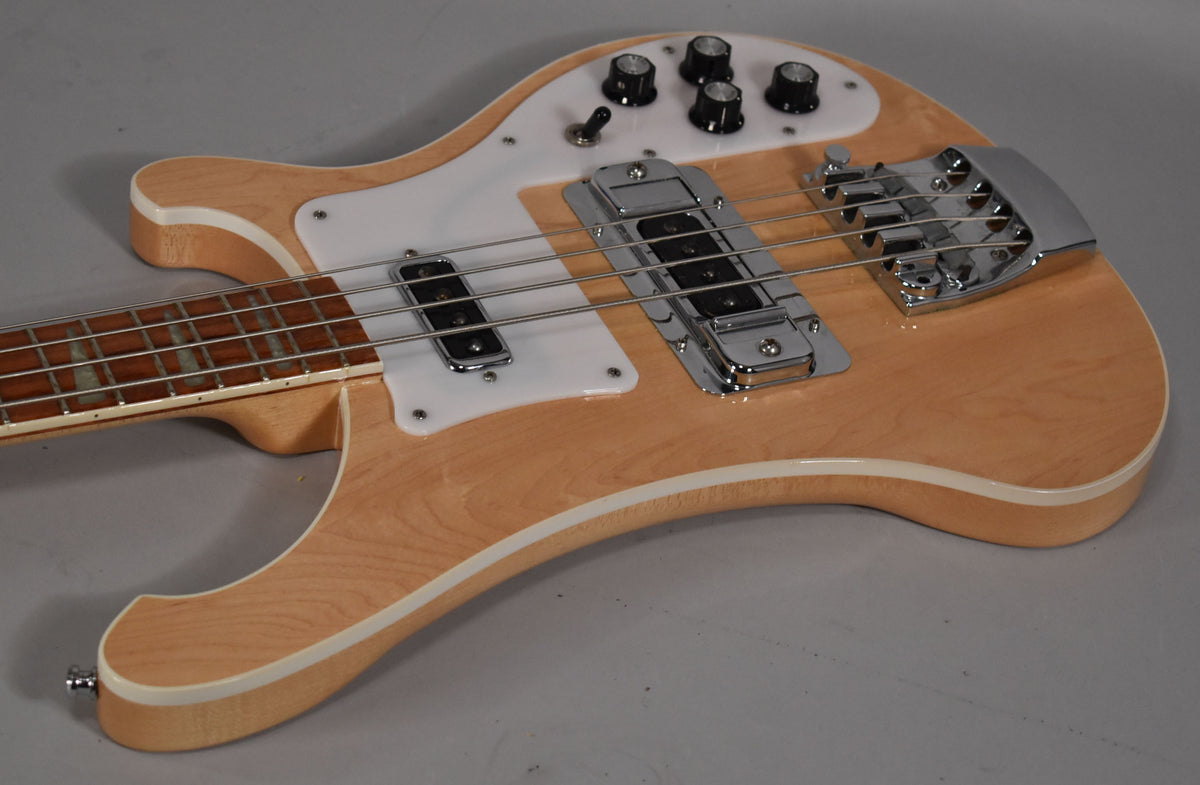 Maple-finished bass, angled from the lower bout, showing the white pickguard, chrome bridge, pickups, and four black control knobs.