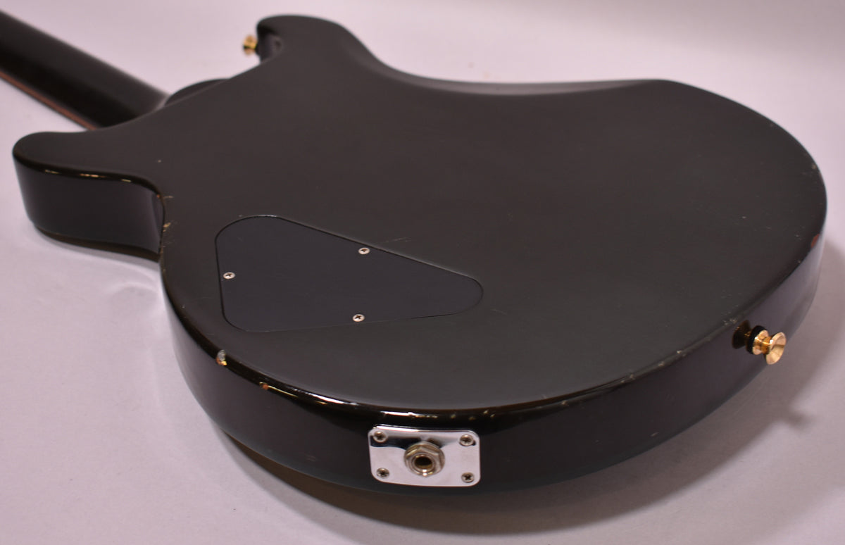 The guitar's emerald green back, angled from the neck, shows a control cavity cover, output jack, and gold strap buttons.