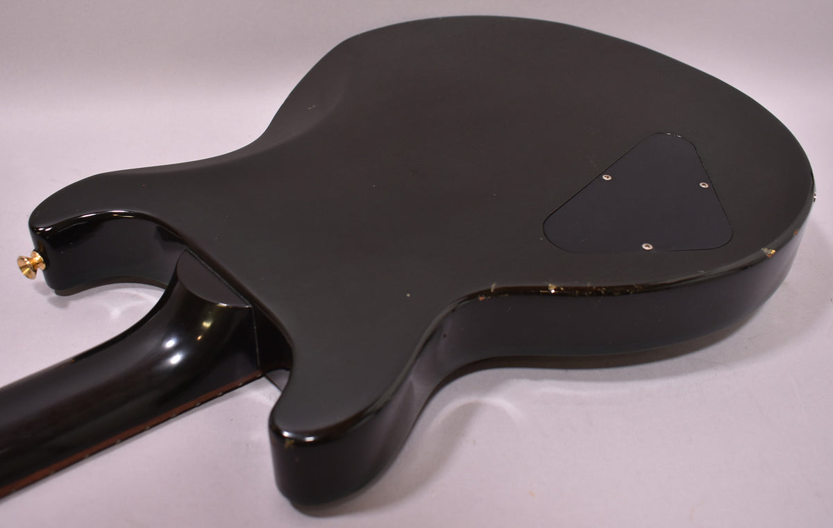 The guitar's dark green back and neck are shown at an angle, revealing a control cavity cover and wear along the body edge.