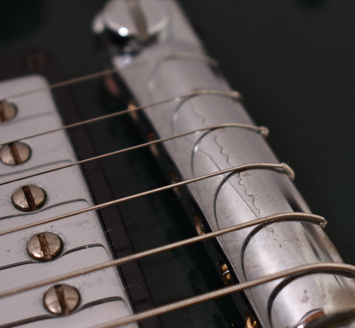 Close-up of the guitar's chrome bridge and tailpiece, showing visible wear, scratches, and some string residue.