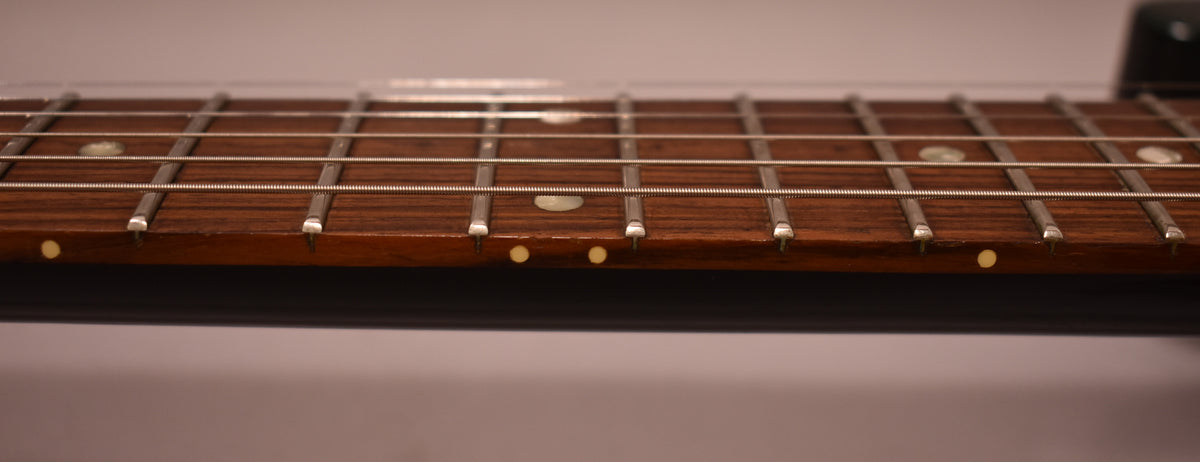 Close-up of the guitar's dark brown fretboard with silver frets, showing white circular inlays and small yellow side dots.