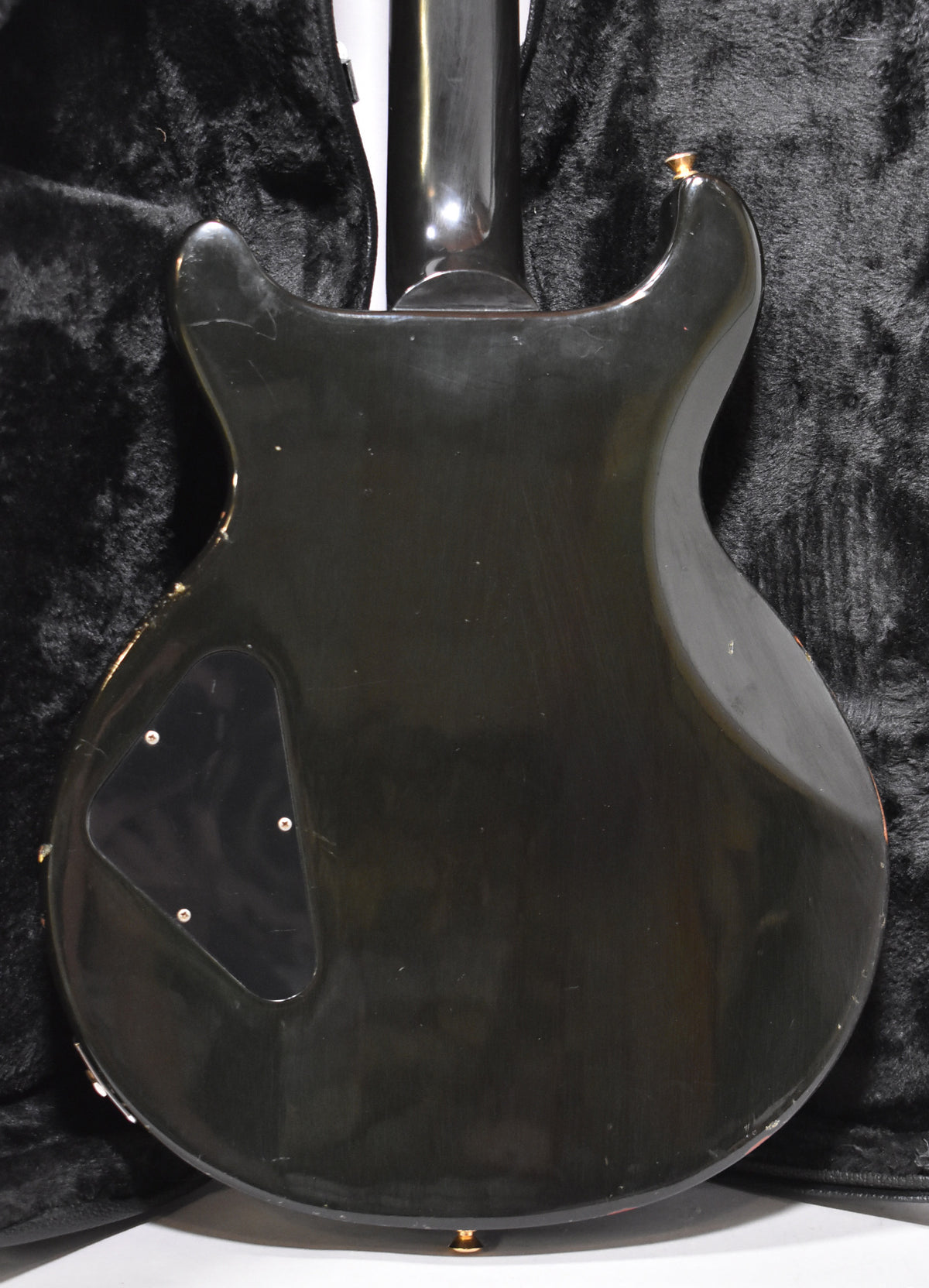 Rear view of a dark green double-cutaway electric guitar with a glossy finish, showing wear, scratches, and a control cavity cover.