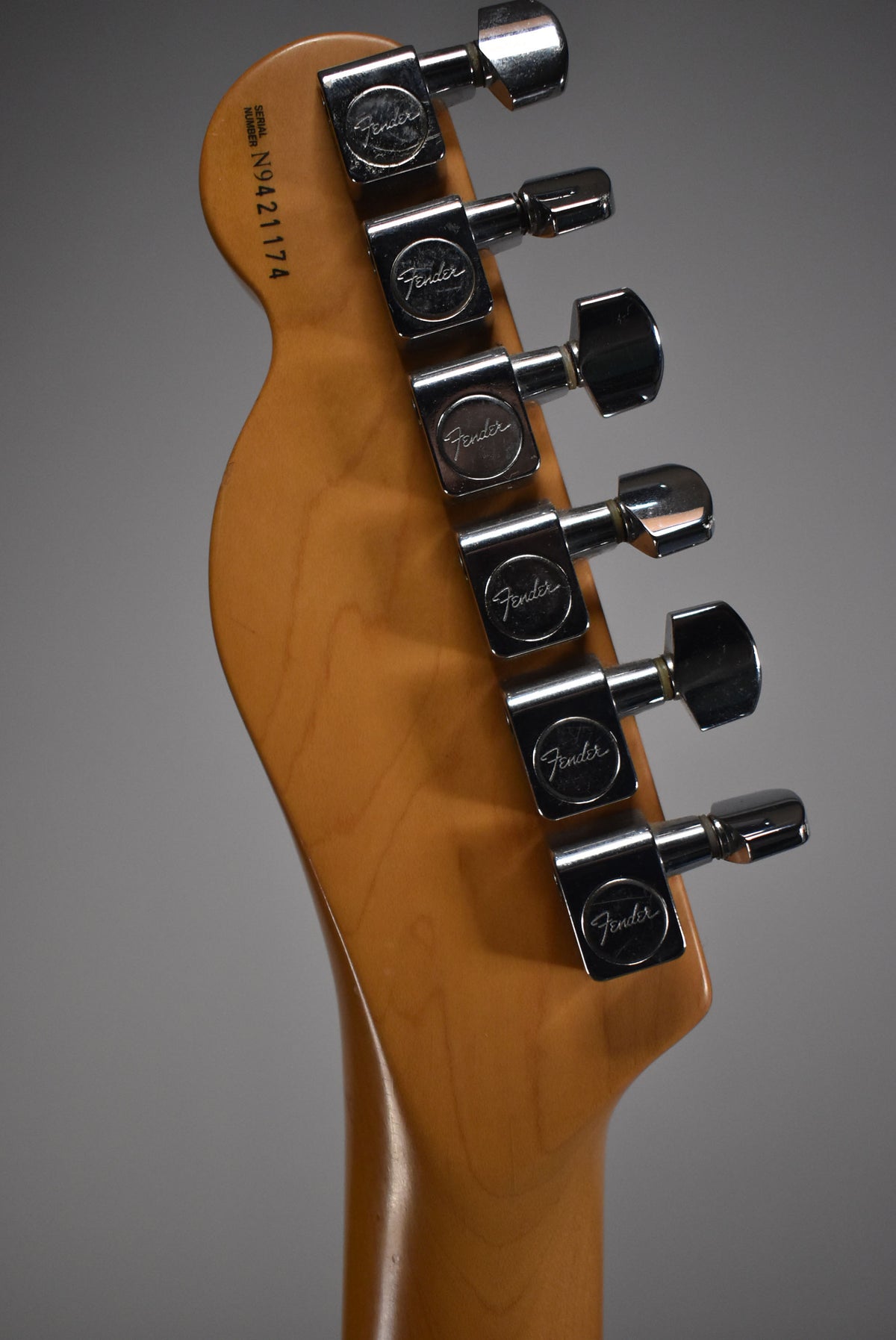 The guitar's headstock, with a light brown finish, is angled to the left, showing six chrome tuning pegs with light wear.