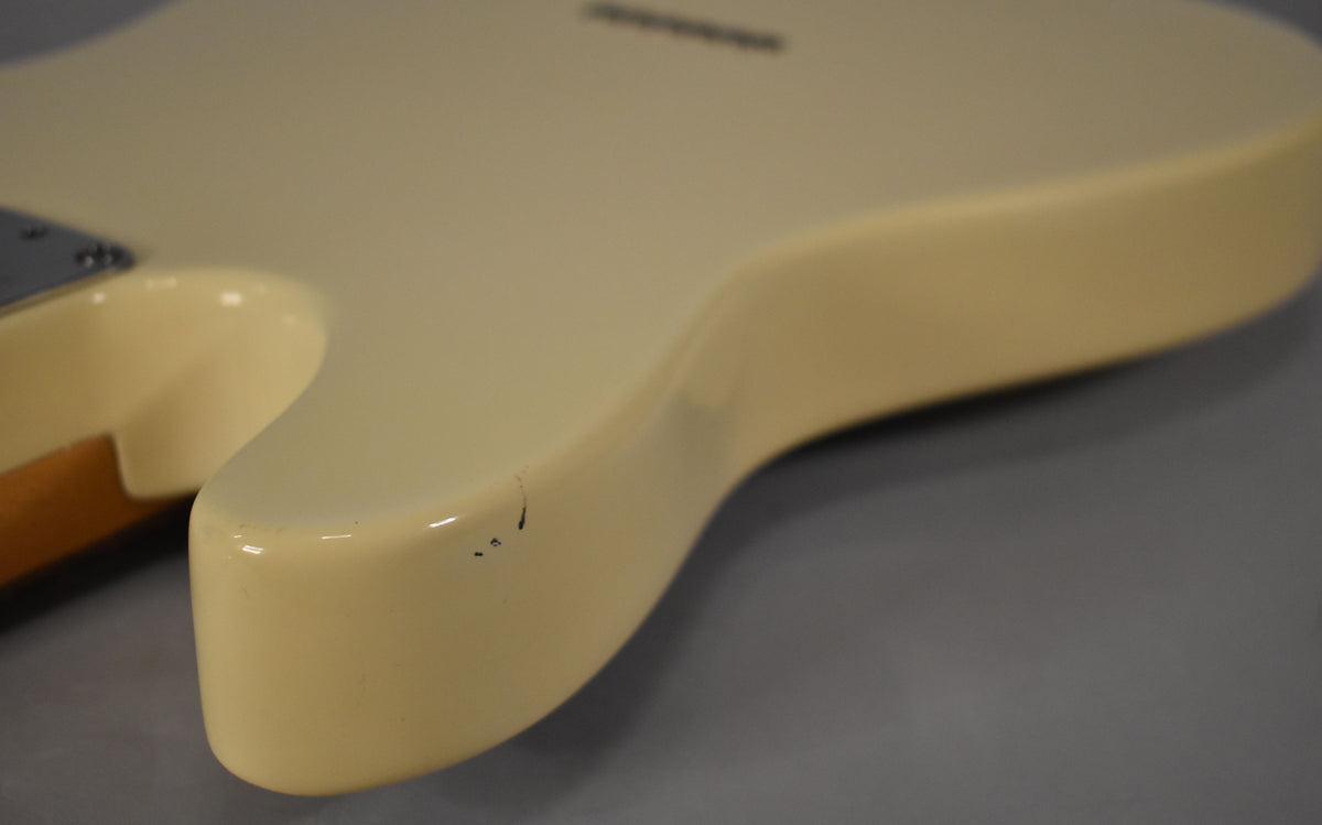 Close-up of the Telecaster's lower bout in Olympic White, showing a few small black chips and scuffs on the curved edge.