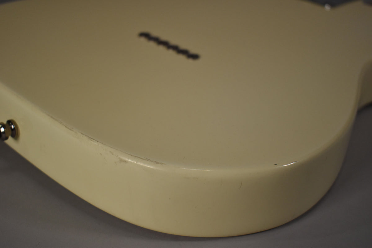 The Olympic White Telecaster's lower bout, viewed from the back, shows light scuffs and a few small dings along the edge.