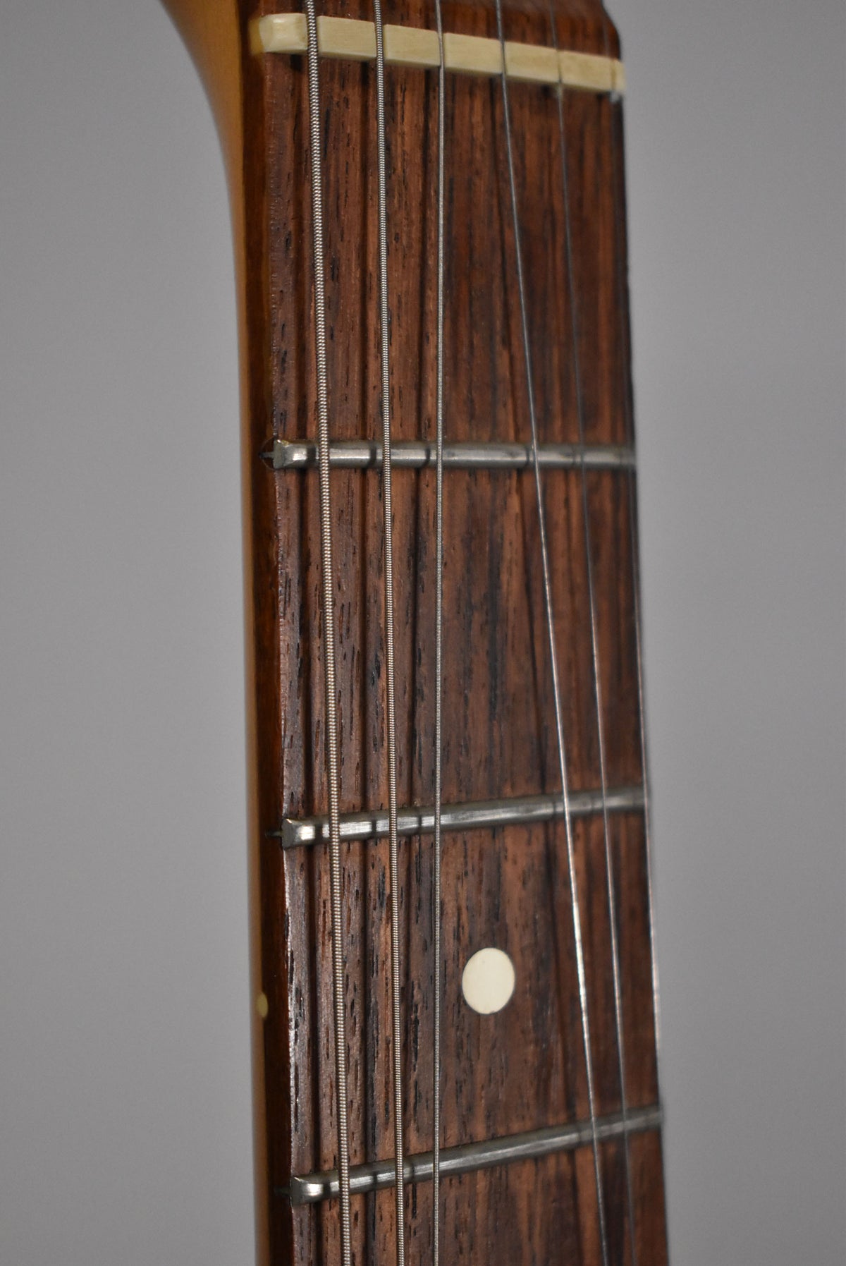 Close-up of the dark rosewood fretboard with white dot inlays, showing some wear on the frets and a light ding on the neck binding.