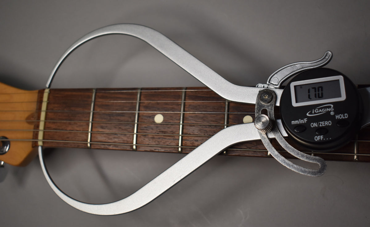 A digital caliper measures the guitar's dark rosewood fretboard, showing a 1.70-inch nut width.