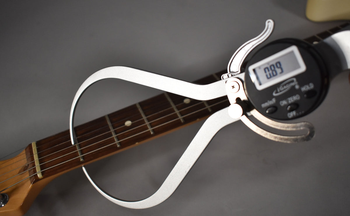 A digital caliper measures the Olympic White Telecaster's dark rosewood fretboard at the nut, displaying "0.89" on its screen.