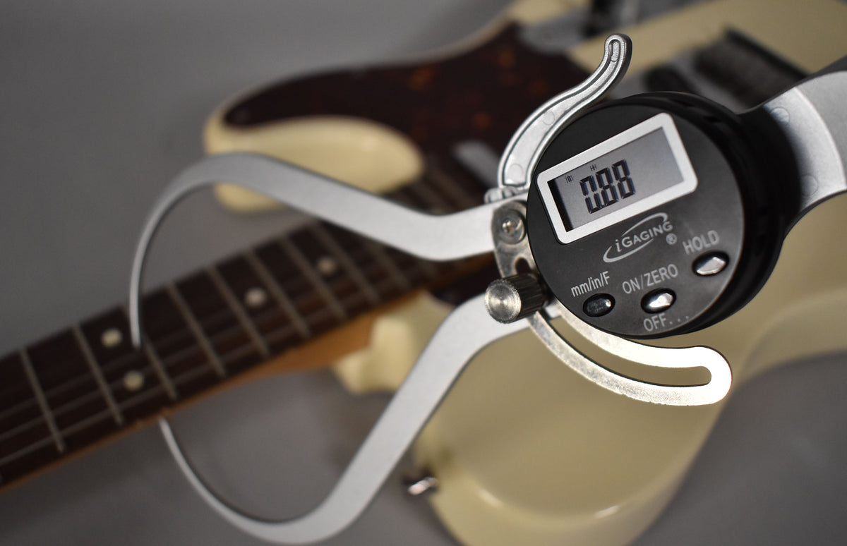 A digital caliper measures the Olympic White Telecaster's fretboard, showing dark wood and dot inlays.