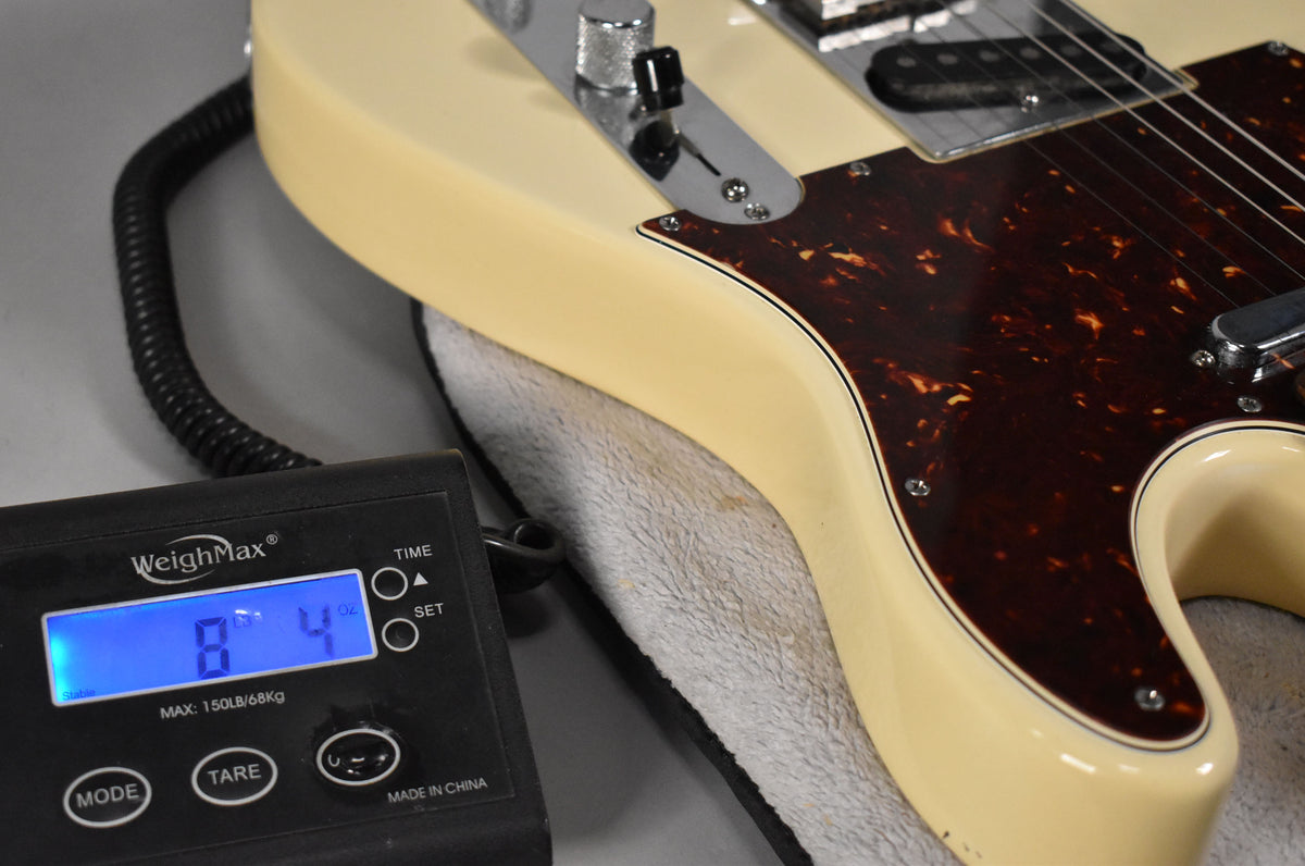 Close-up of the guitar's lower body, showing its Olympic White finish, tortoiseshell pickguard, and a digital scale displaying 8 lbs 4 oz.