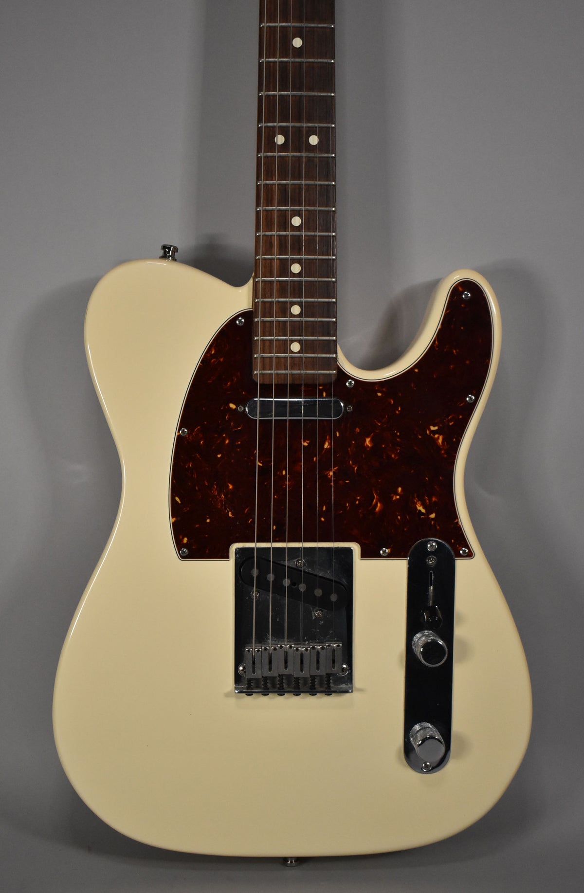 Olympic white Telecaster, body and neck framed vertically, with a tortoiseshell pickguard and chrome hardware.