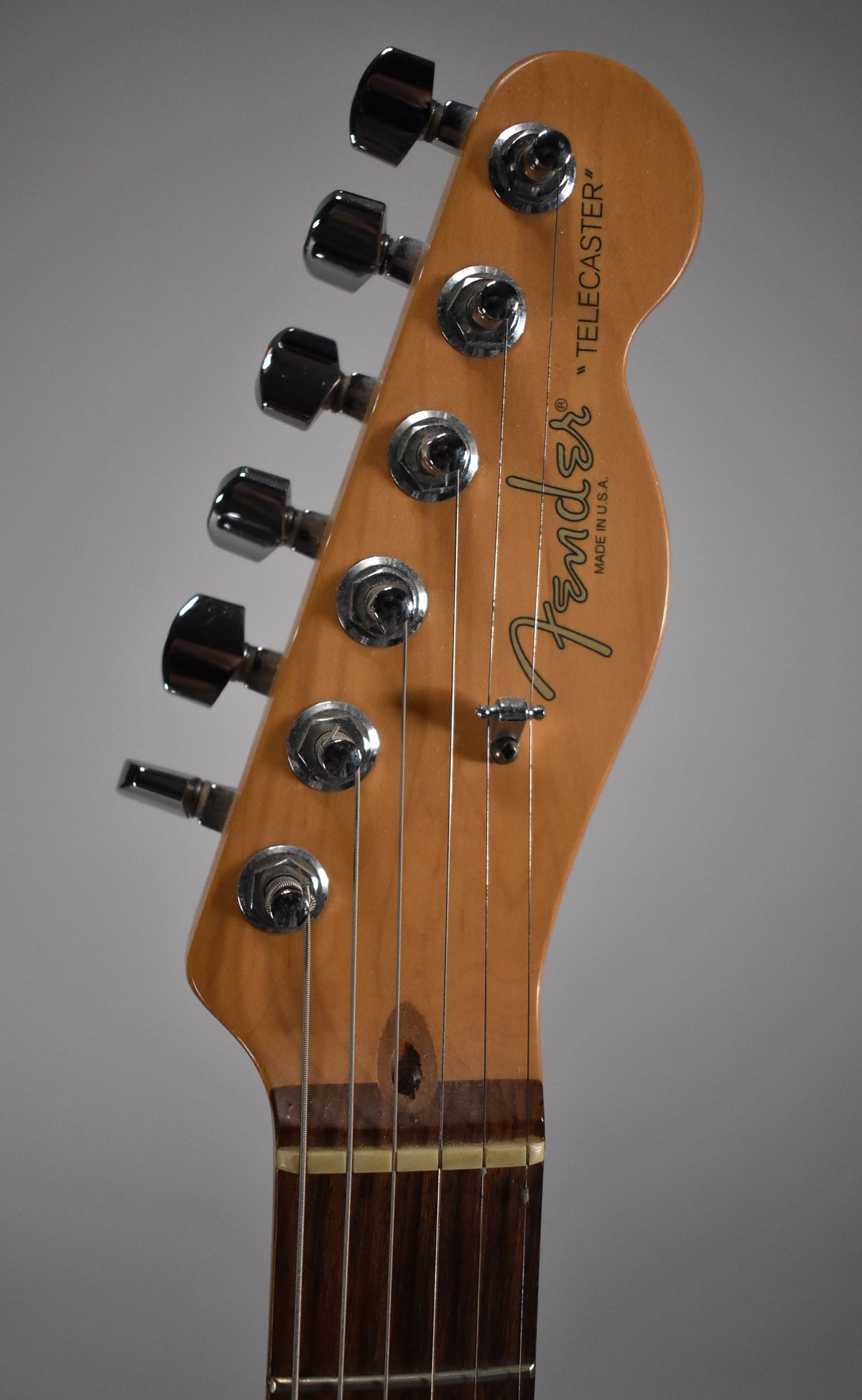 Close-up of the guitar's headstock, showing six chrome tuners, a string tree, and a dark circular ding near the nut.