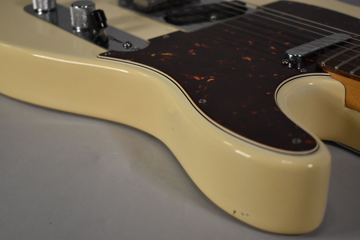 Close-up of the lower bout of an Olympic White Telecaster, showing the tortoiseshell pickguard, chrome control plate, and minor chips on the edge.
