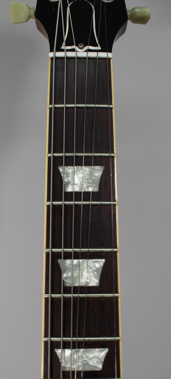 Close-up of the dark rosewood fretboard with trapezoid mother-of-pearl inlays, showing the nut and tuning pegs.