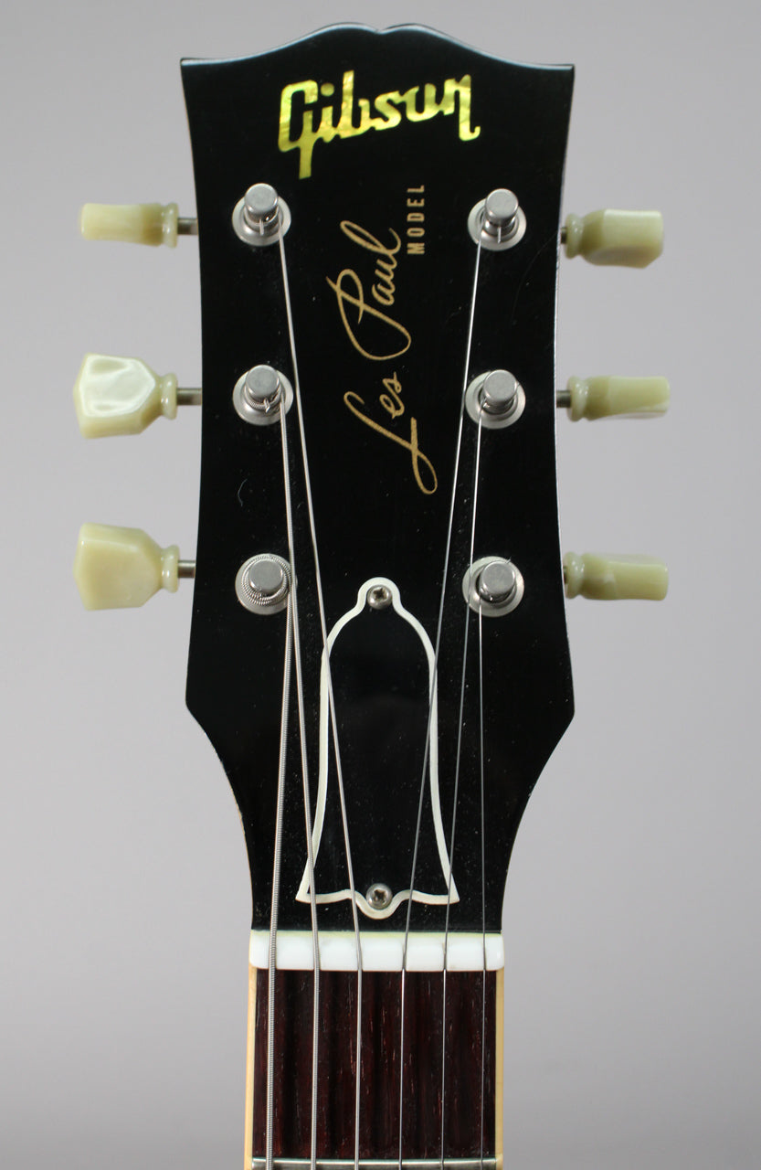 The black headstock, with cream tuning pegs and gold lettering, is framed from the top, showing the nut and fretboard.