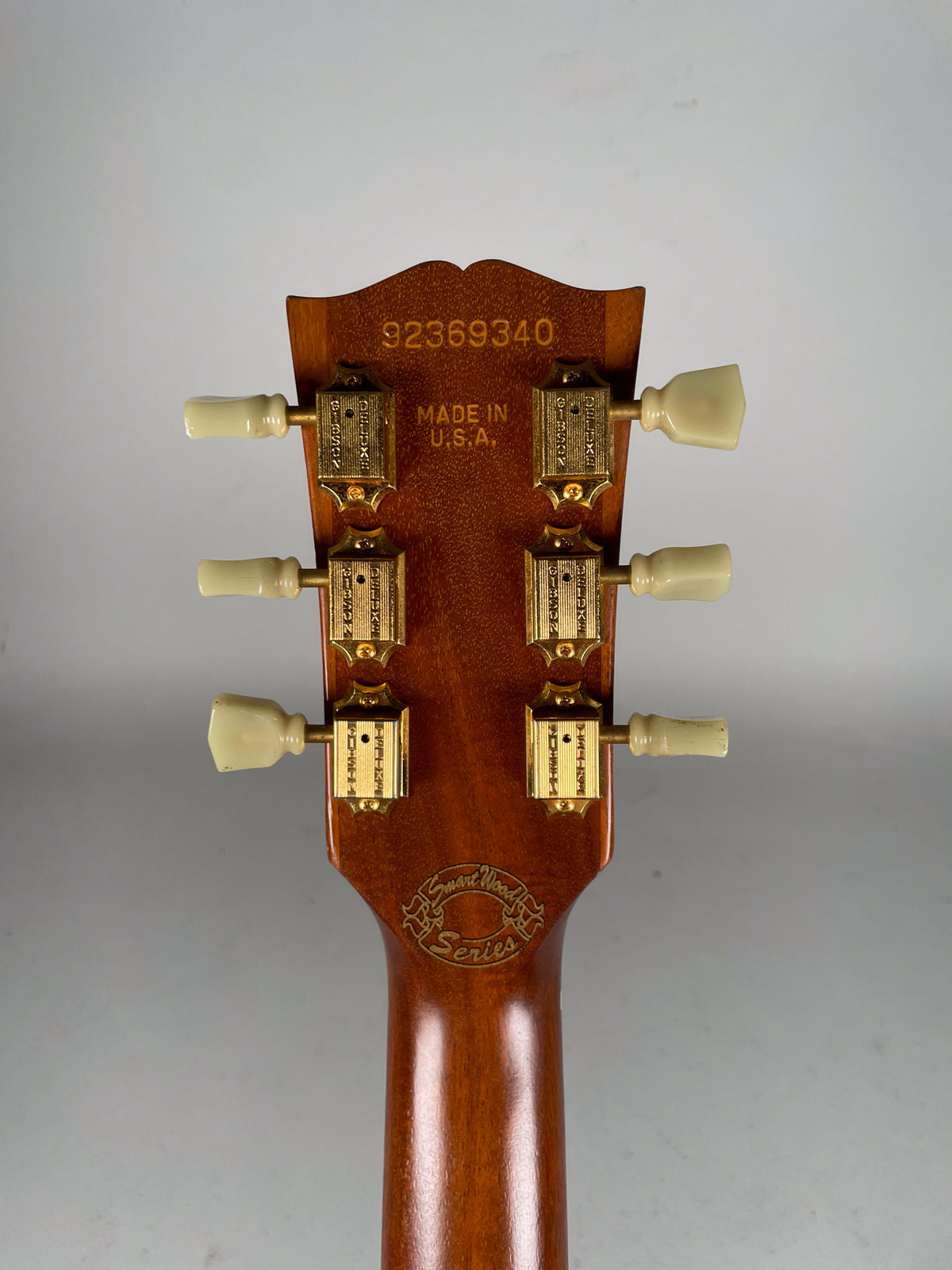 The back of a guitar headstock with a natural wood finish, six gold tuners, and cream-colored tuning pegs.