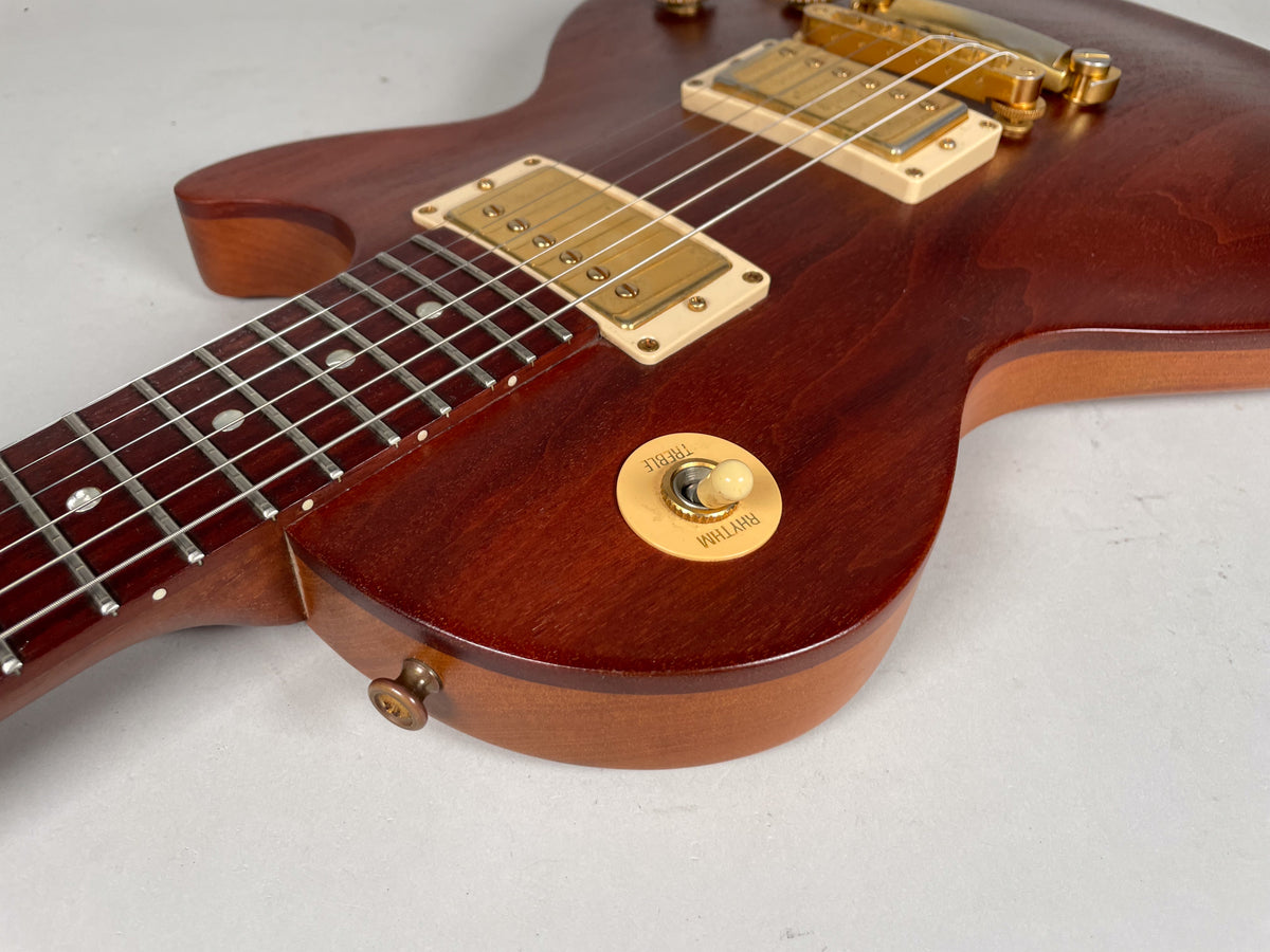 Upper body of a natural finish mahogany guitar, showing the neck joint, gold humbuckers, and cream Rhythm/Treble switch.