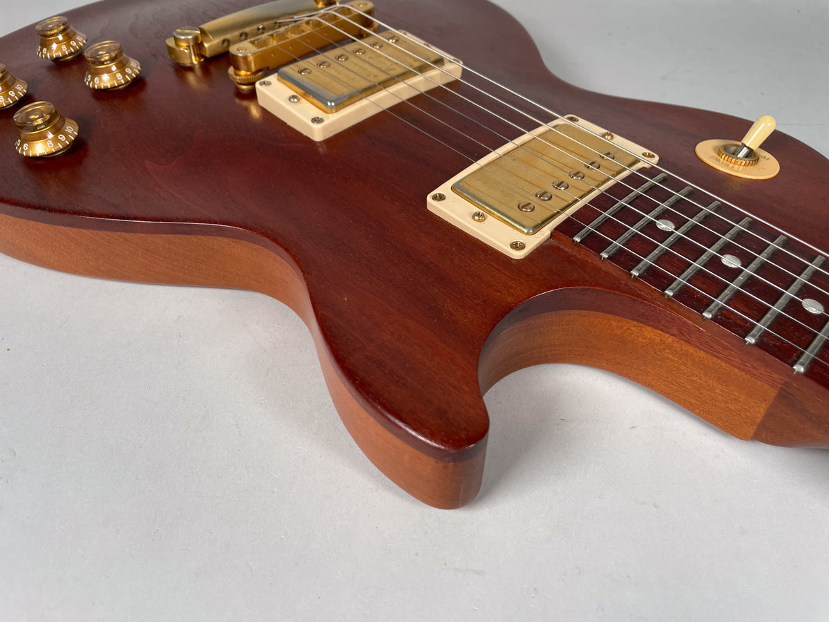 Close-up of the guitar body, showing the natural wood grain, gold hardware, cream pickup rings, and four gold control knobs.