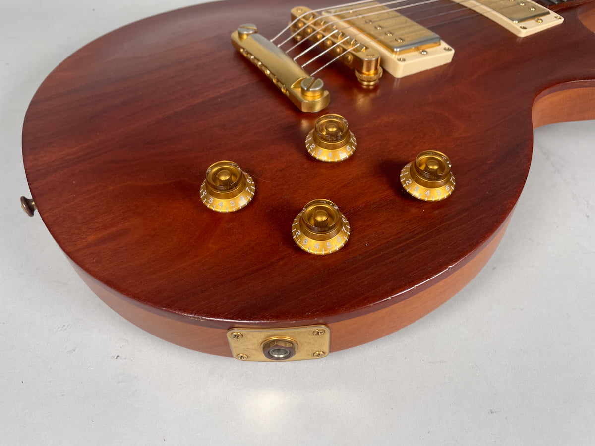 Close-up of the guitar's lower body, showing the natural wood grain, four gold top hat knobs, and the input jack with a worn gold plate.
