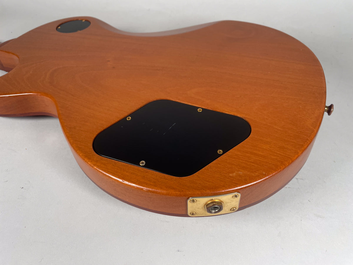 The guitar's natural finish back, showing the control cavity cover, output jack, and a small ding near the lower bout.