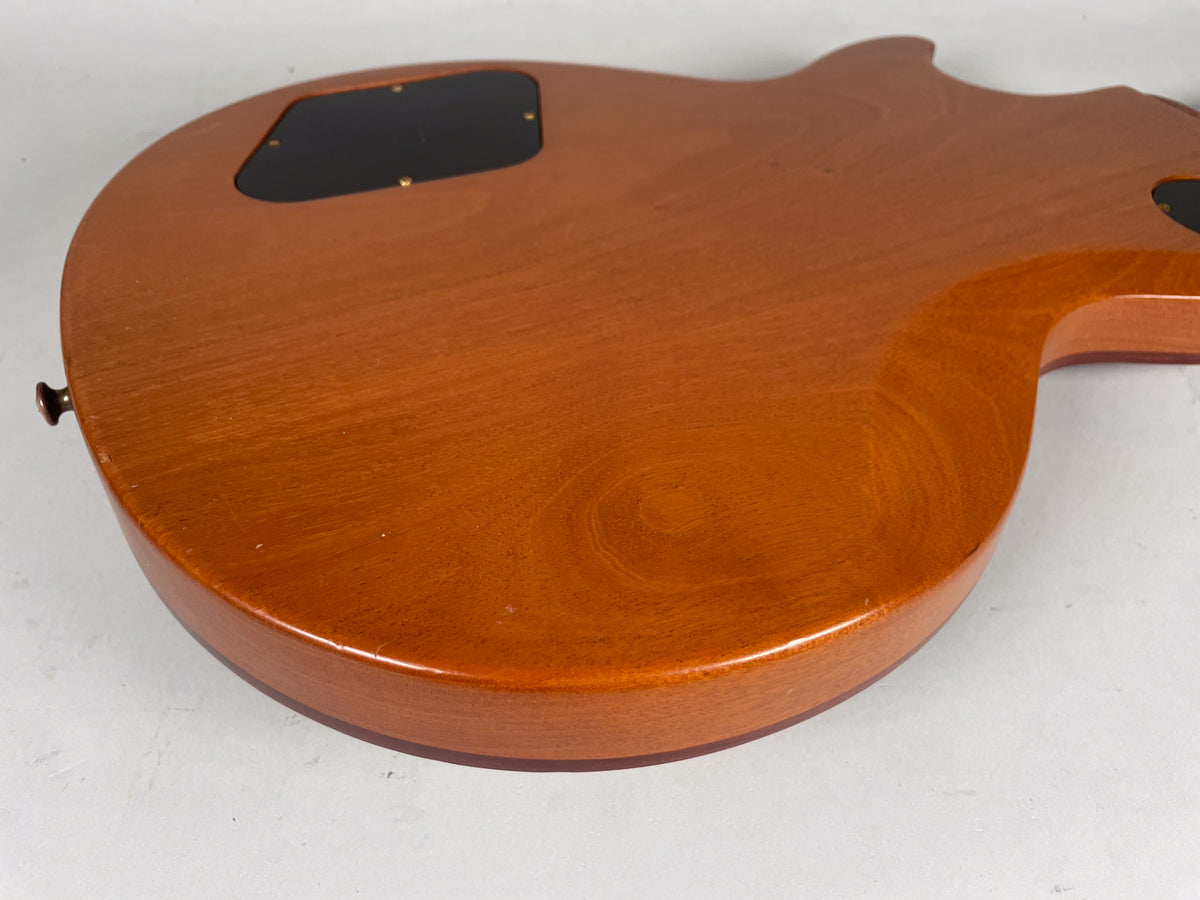 The back of a natural finish guitar body, showing a black control cavity cover and light wear on the lower bout.