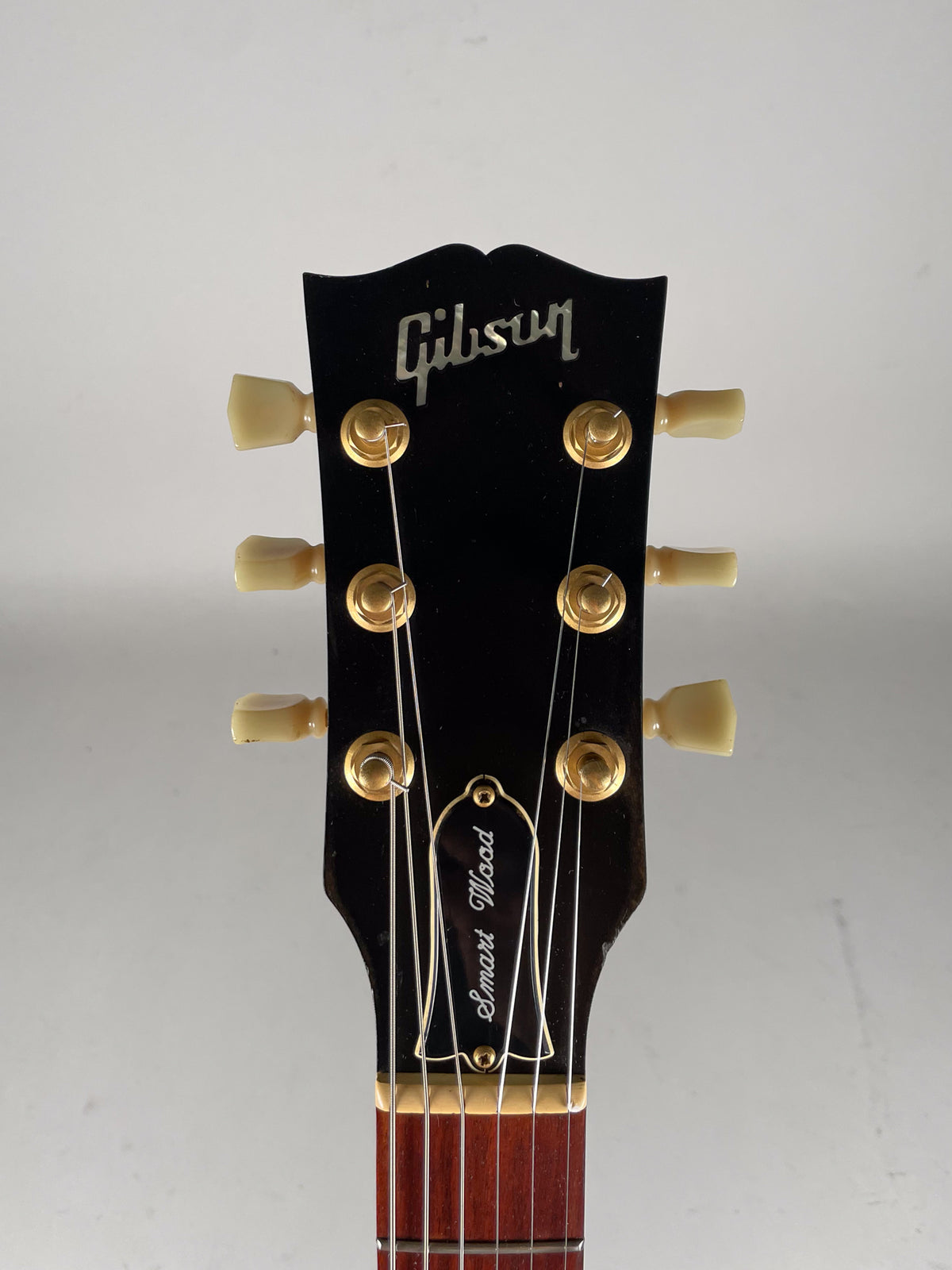 Close-up of the black headstock with gold tuners and cream buttons, showing some wear on the lower right button.