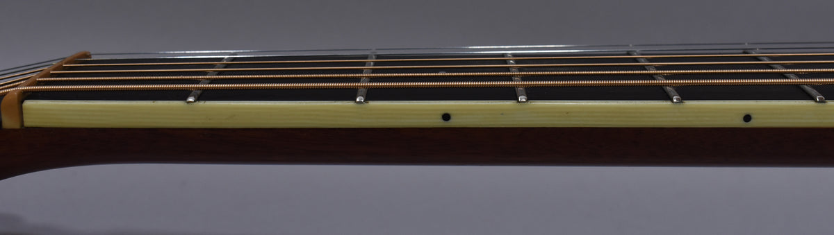 The guitar's dark brown neck and light cream binding are visible from the side, with strings and frets running across the top.