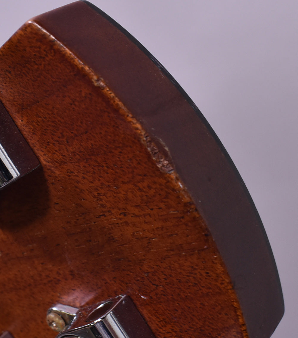 Close-up of the guitar's lower bout, showing a large chip and several smaller dings on the dark brown finish.