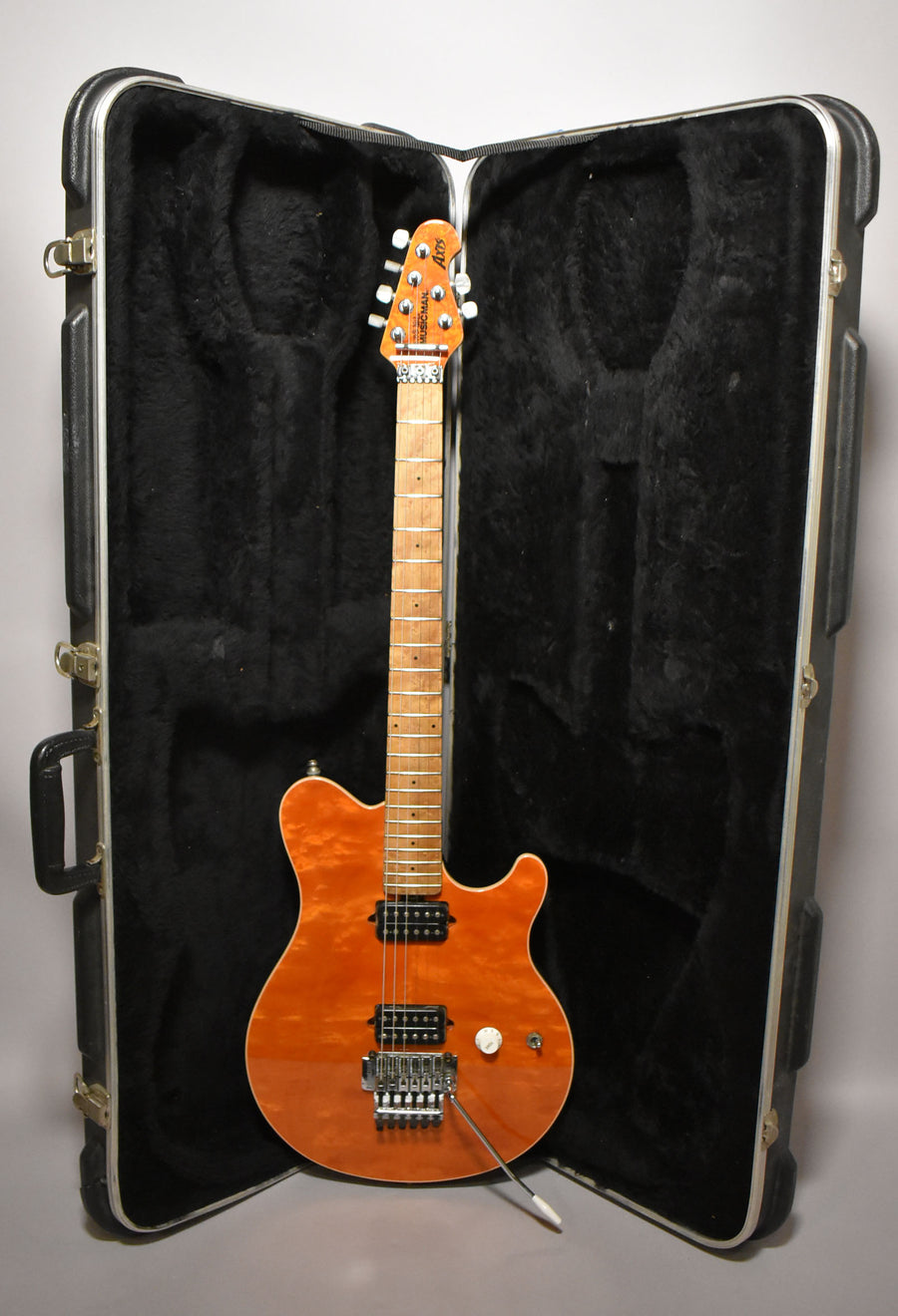 Full-length view of a glossy orange flame-top guitar with a maple neck, black humbuckers, and a chrome Floyd Rose tremolo, standing in its open black hard case.