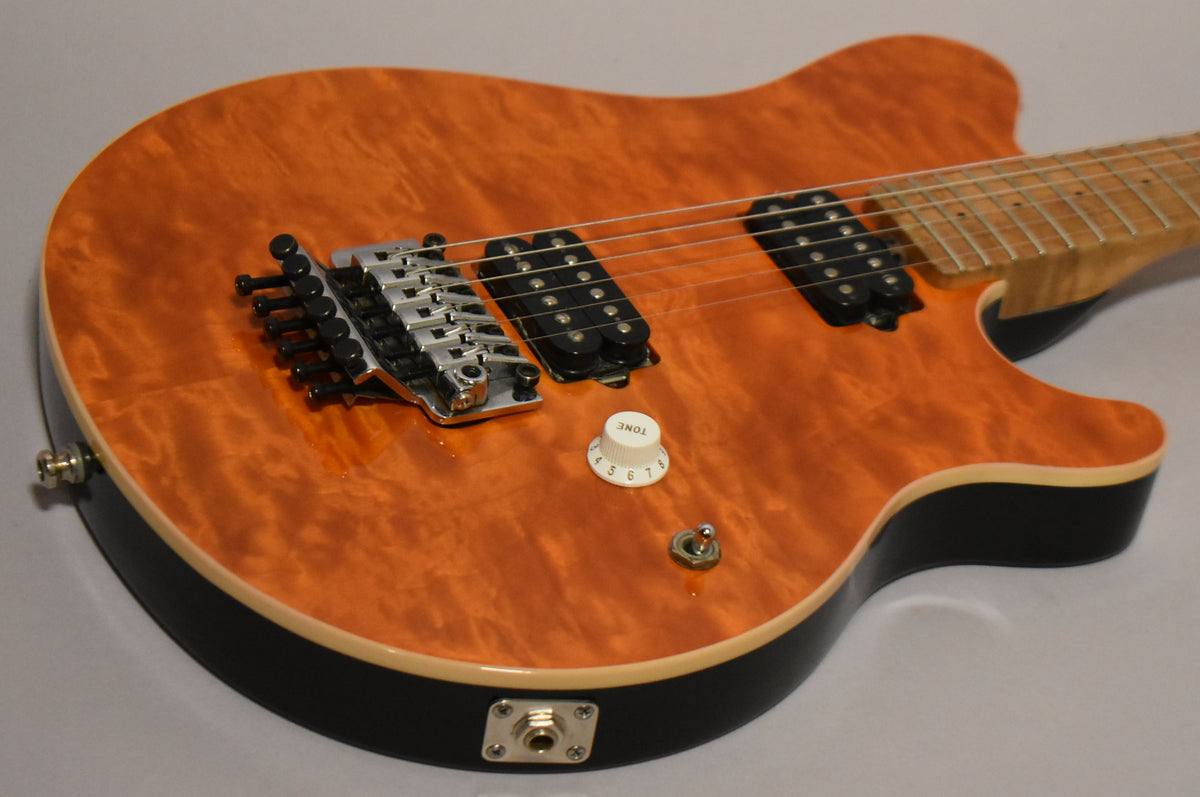 The upper body of an orange flame maple top guitar with black sides, showing a chrome Floyd Rose bridge, two black humbuckers, and a white tone knob.