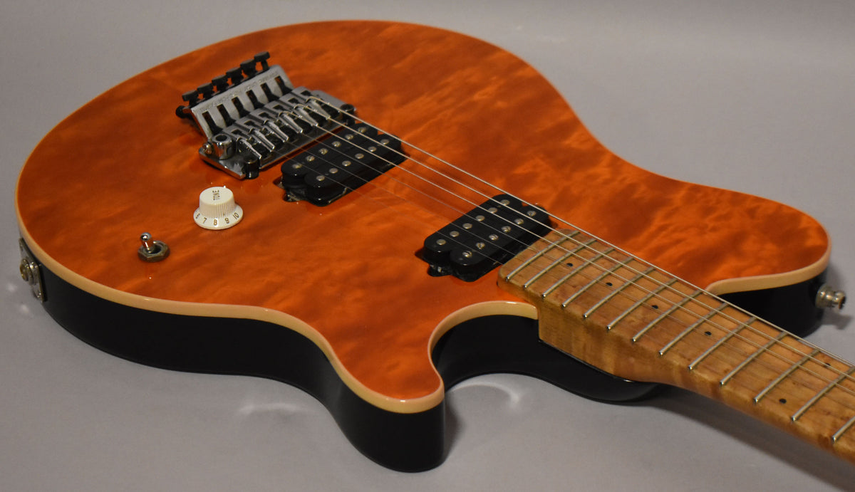 The guitar's flame maple top in orange burst, black body, and maple fretboard are visible from the upper bout to the neck joint.