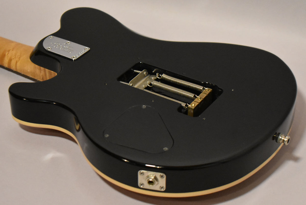 The guitar's black gloss back shows a tremolo spring cavity, control plate, output jack, and a light-colored binding around the edge.