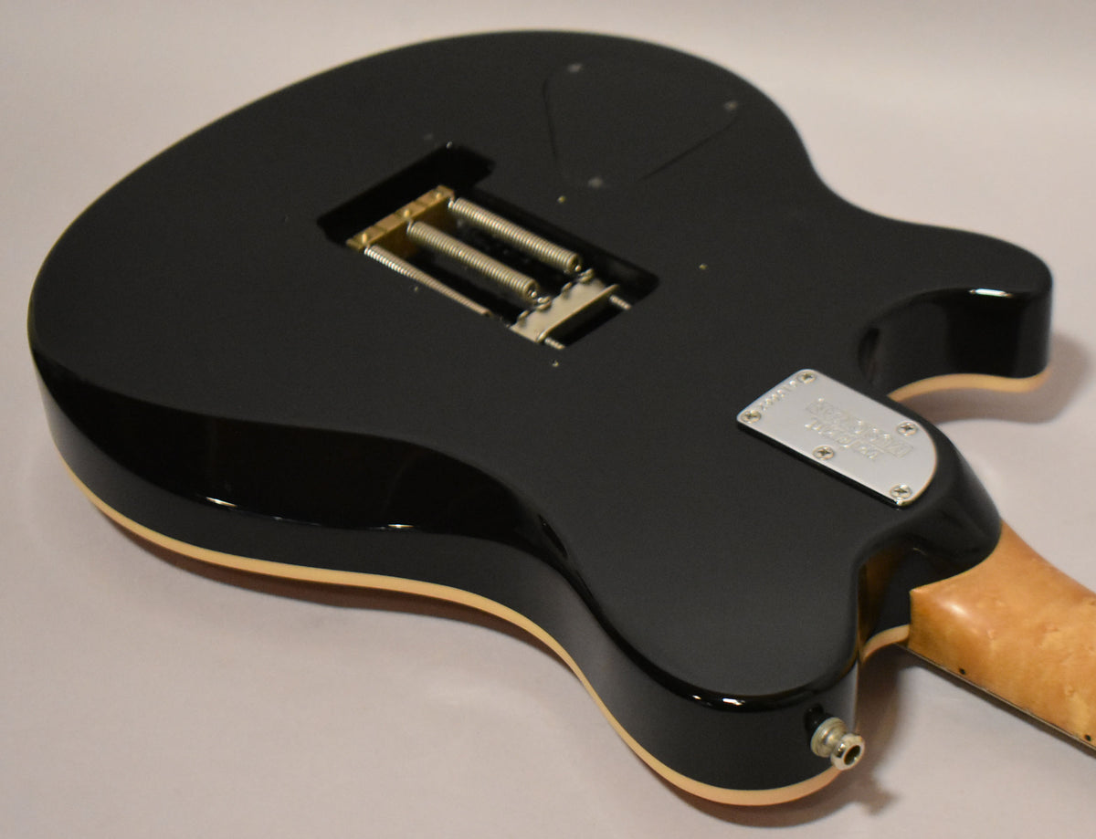 The guitar's glossy black back, with cream binding, shows a tremolo spring cavity and a chrome neck plate, with a maple neck.