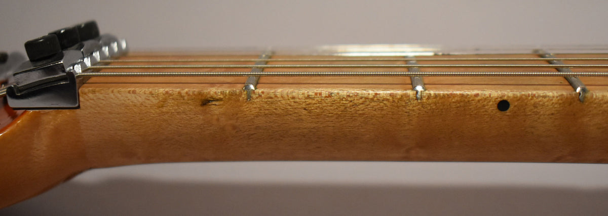 Close-up of the natural maple fretboard and neck, showing a locking nut, frets, and a small ding near the first fret.