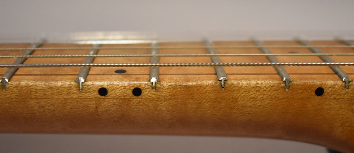 Close-up of the light brown maple fretboard and frets, showing dark dot inlays and some wear along the edges.